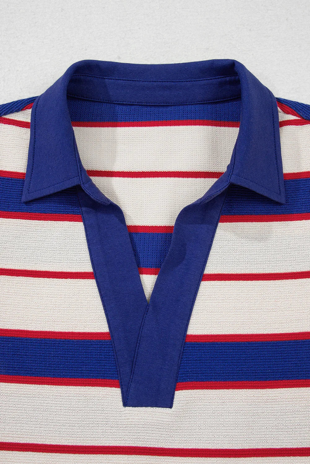 Close-up of a knit shirt with blue collar and red, blue, and white horizontal stripes.