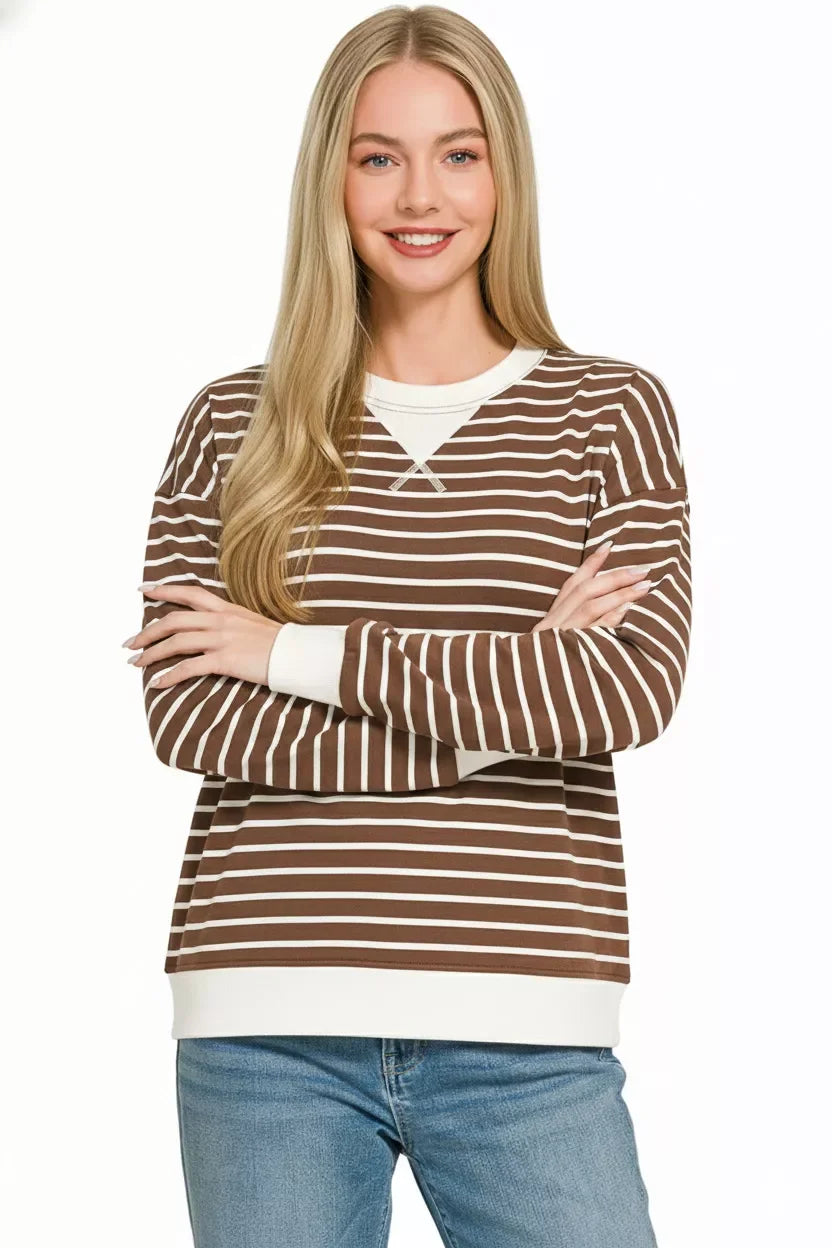 Woman wearing a brown and white striped long sleeve sweater with relaxed fit and blue jeans