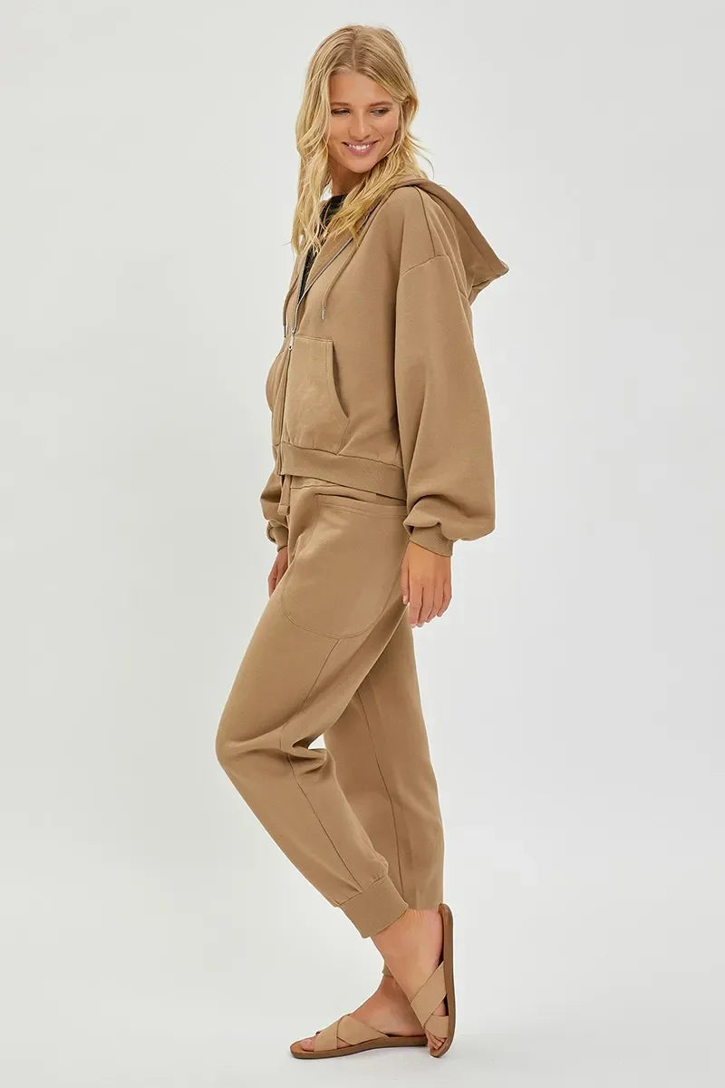 Woman wearing tan hooded zip-up sweatshirt and matching joggers with sandals, side view