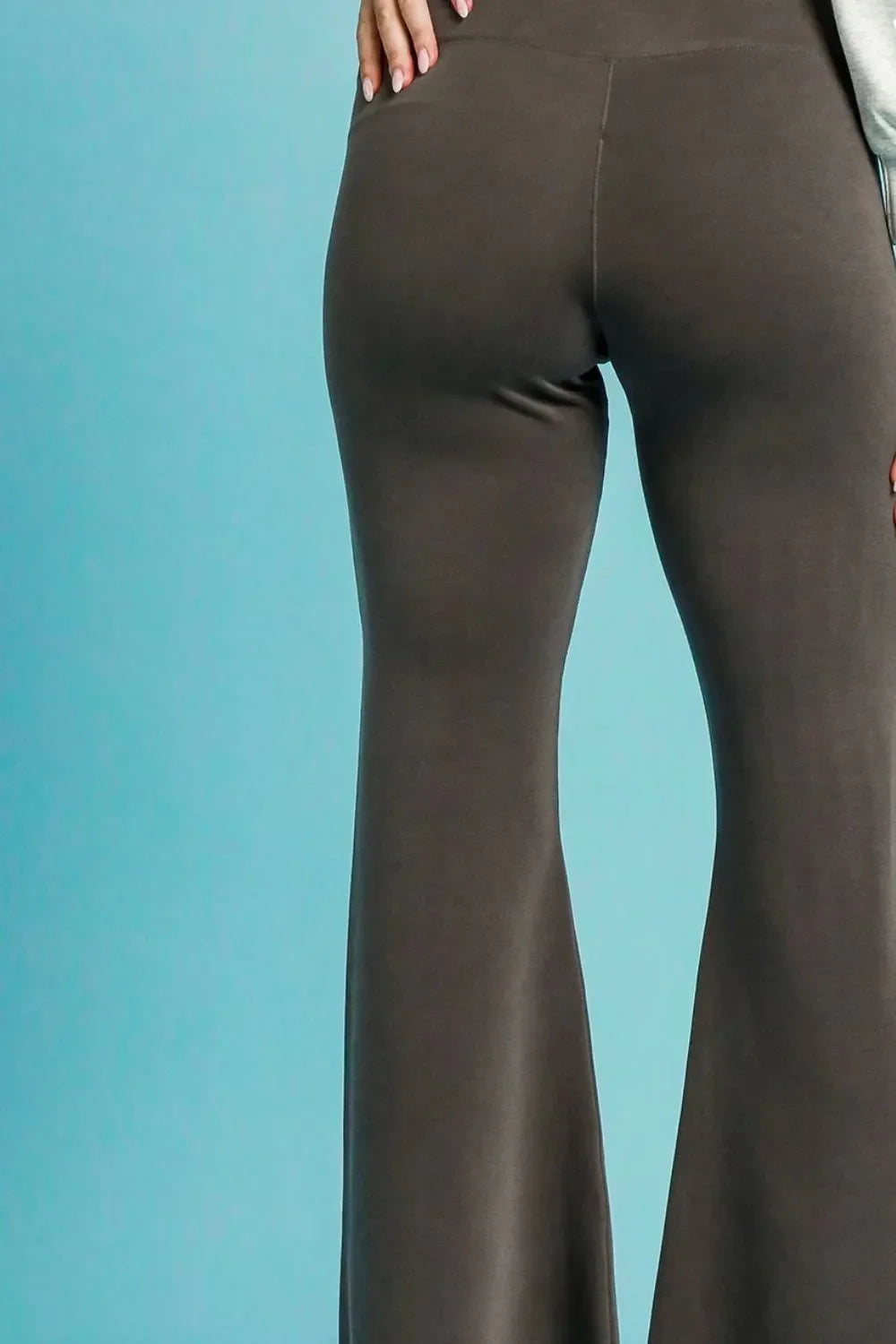 High-waisted taupe flared pants with relaxed fit on model against blue background