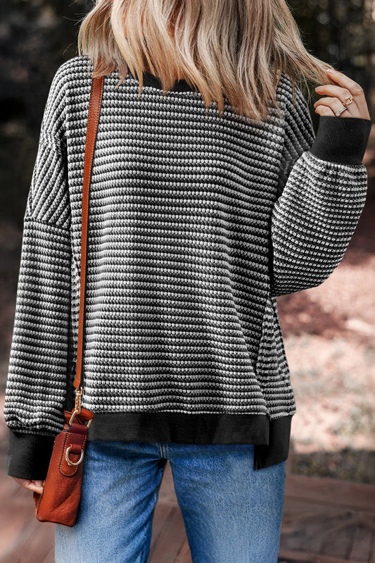 Woman wearing a black and white striped knit sweater, blue jeans, and brown crossbody bag outdoors.