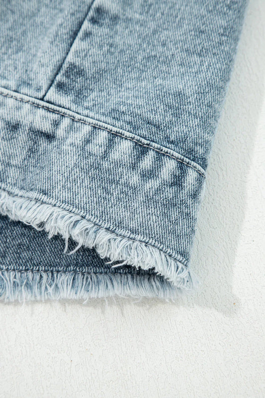 Close-up of light wash denim fabric with raw frayed hem detail on a white surface.