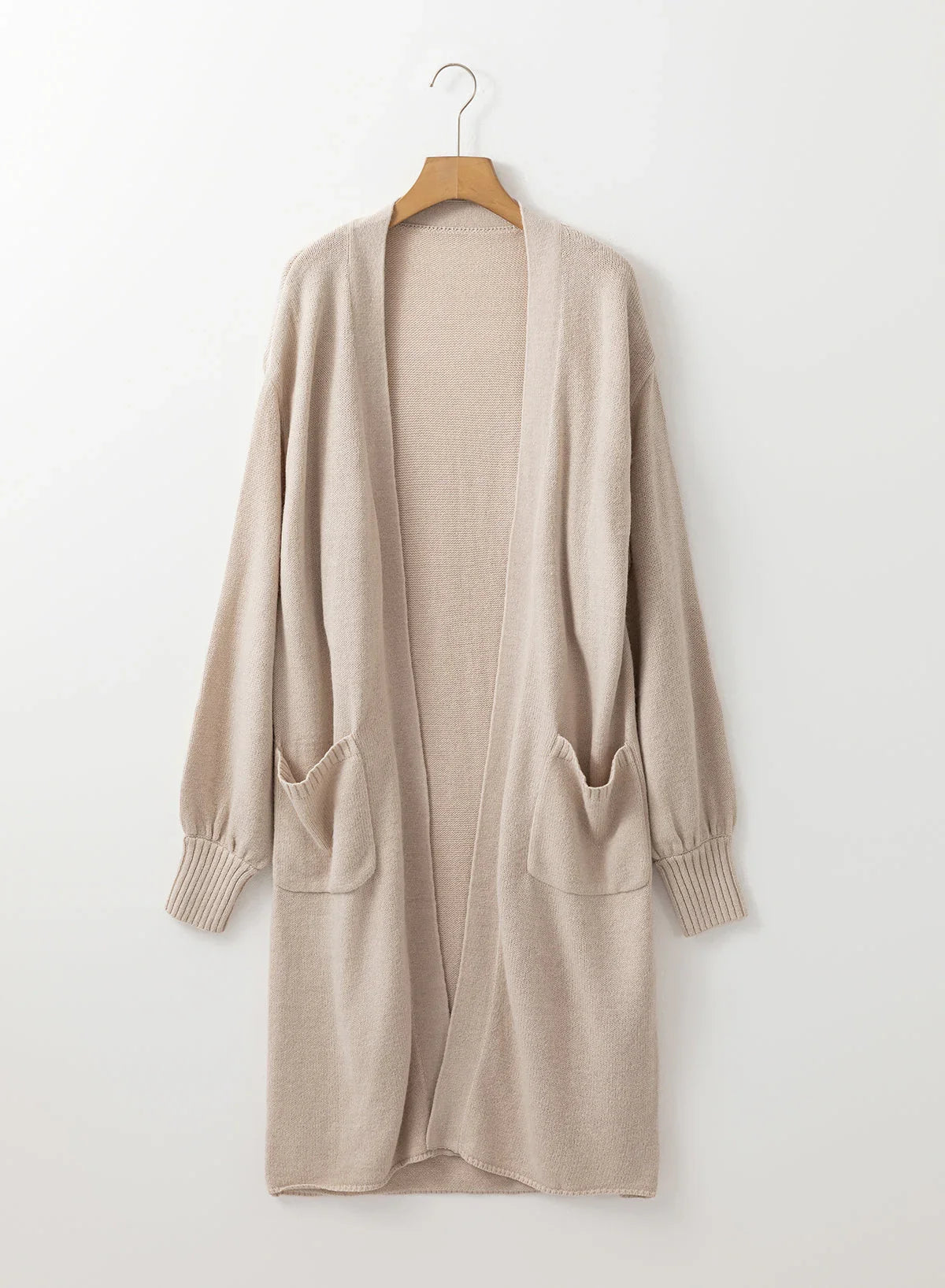 Beige open-front long knit cardigan with pockets and ribbed cuffs on wooden hanger.