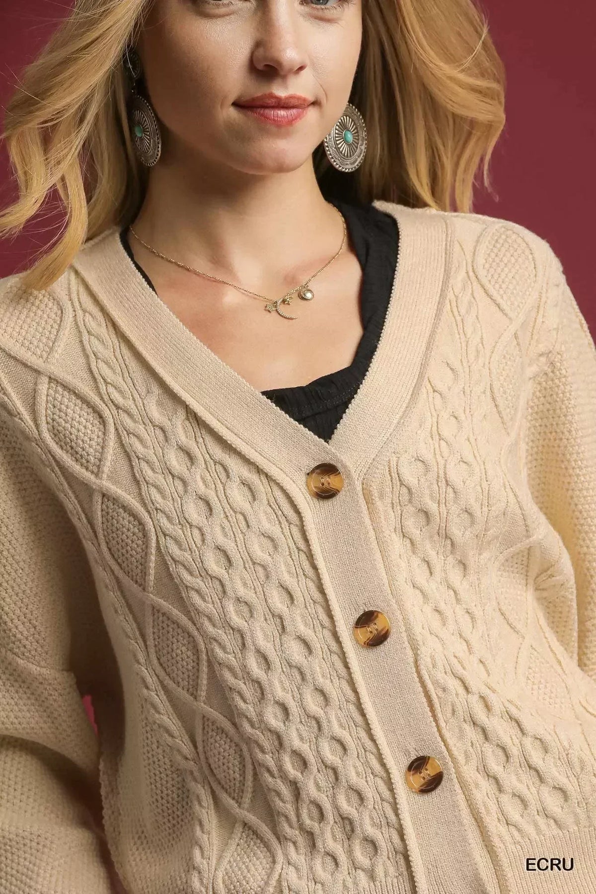 Woman wearing an ecru cable knit cardigan with large buttons and textured pattern.