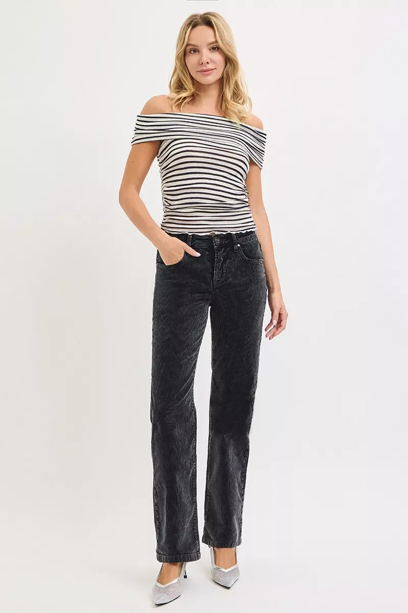 Woman in off-the-shoulder striped top and black high-waisted jeans standing against white background