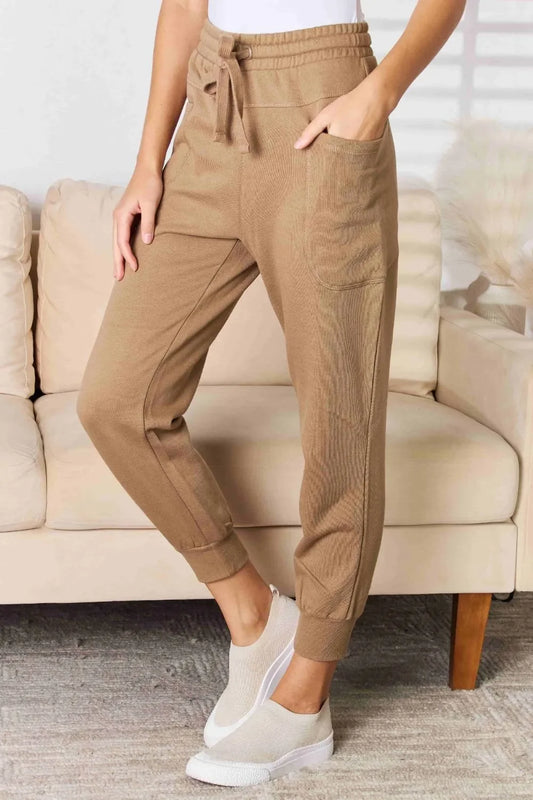 Woman wearing tan jogger pants with drawstring waist and white slip-on sneakers indoors.