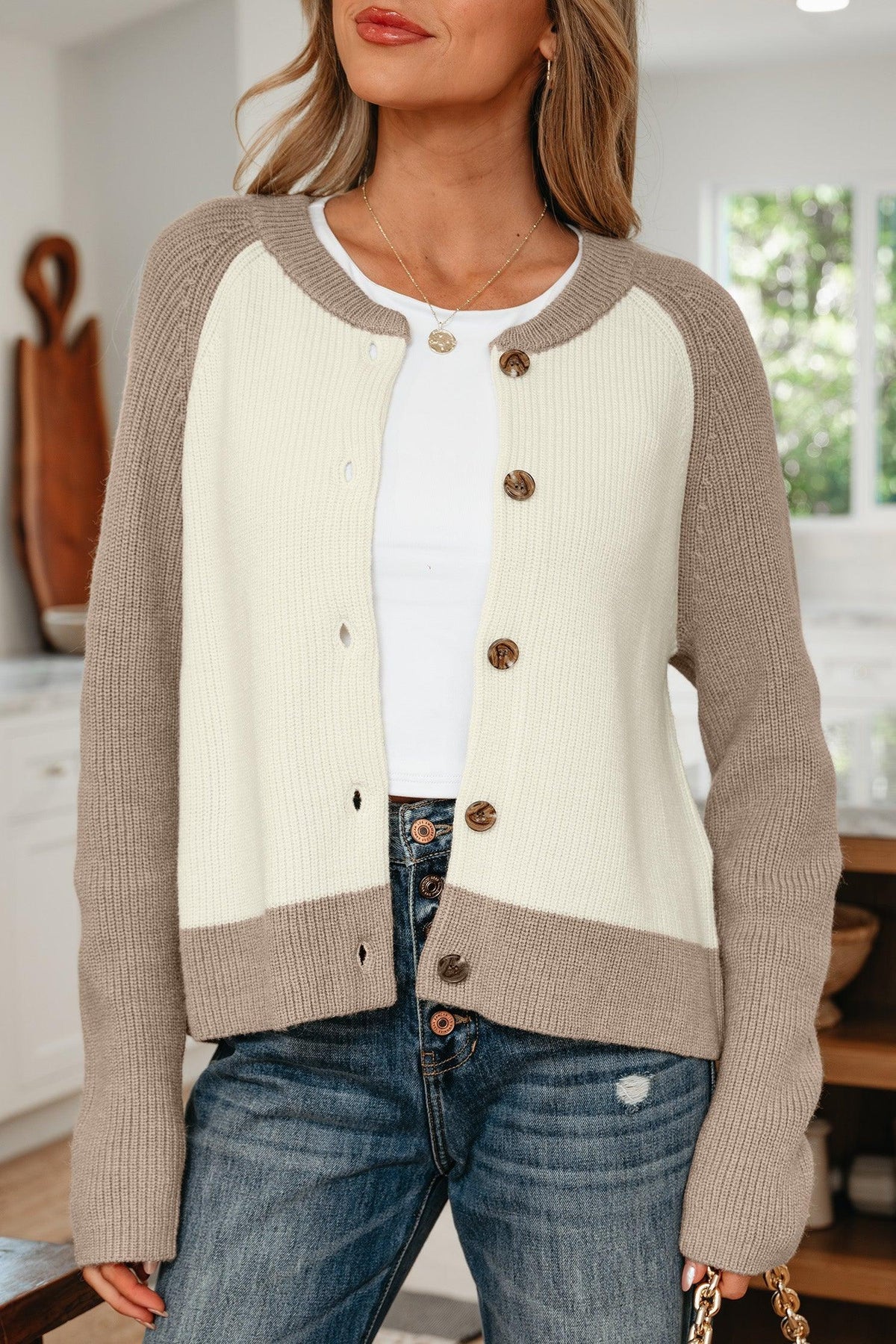 Woman wearing a two-tone knit cardigan with beige sleeves and cream front, paired with jeans