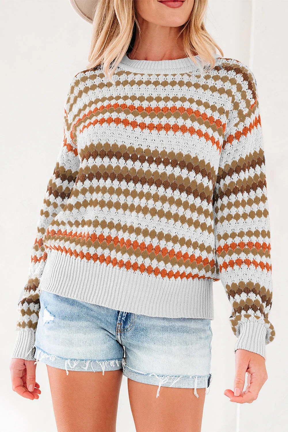 Woman wearing a patterned knit sweater with orange and brown accents and denim shorts.