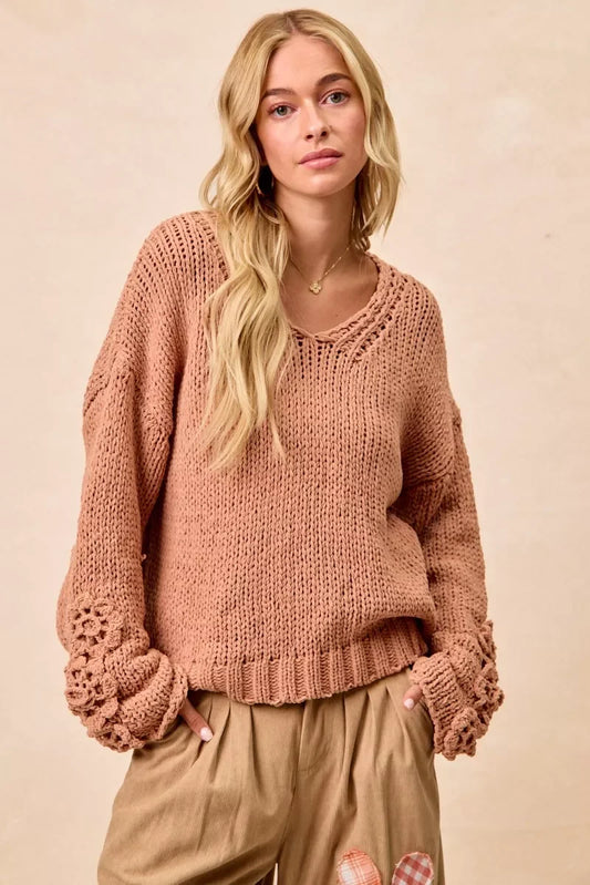 Woman wearing a chunky knit sweater with crochet cuffs and relaxed fit pants in neutral tones