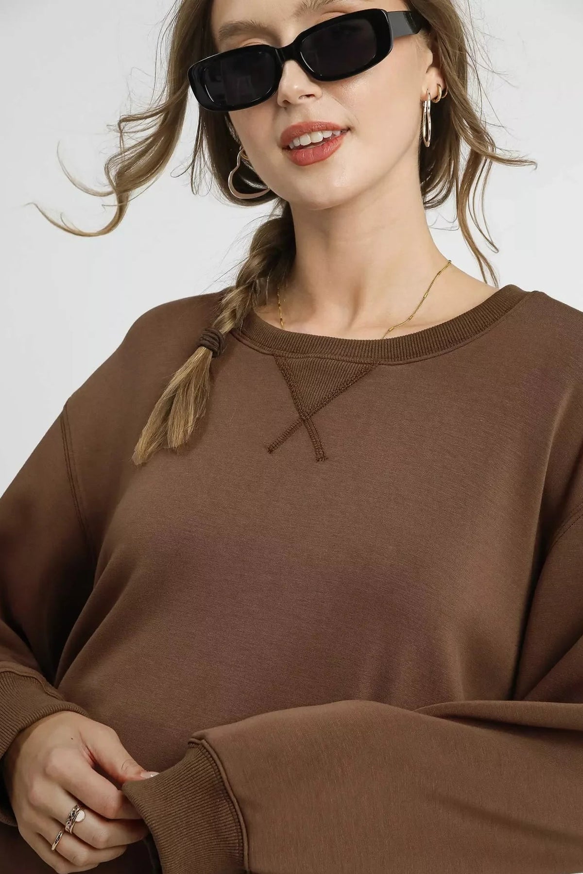 Woman wearing oversized mocha brown sweatshirt, gold jewelry, and black sunglasses