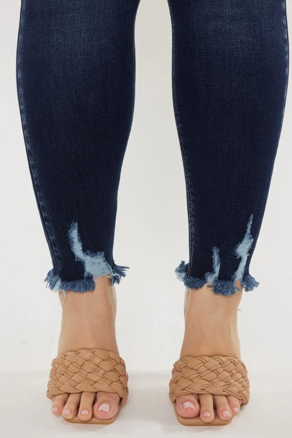Dark wash skinny jeans with raw frayed hems and woven tan slide sandals