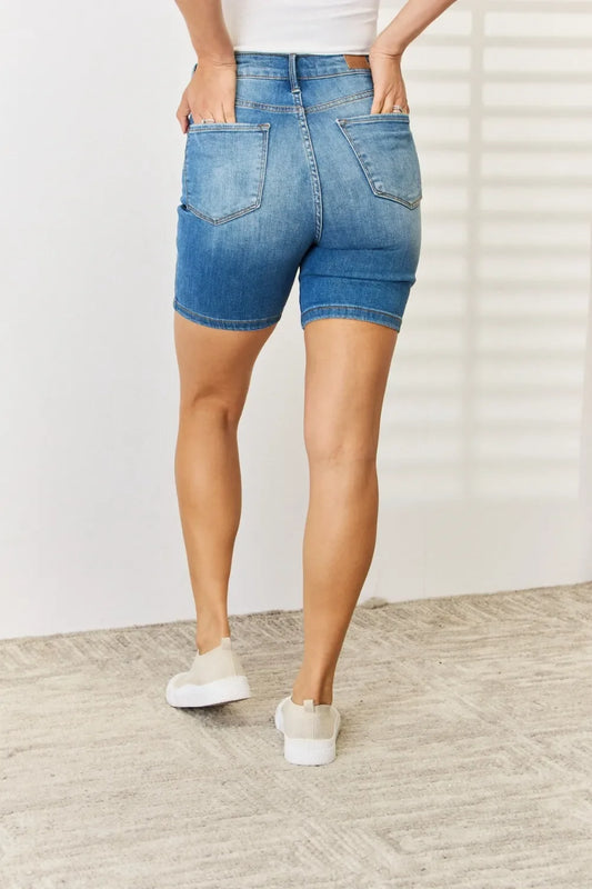 Back view of woman wearing high-waisted denim shorts and casual white sneakers indoors