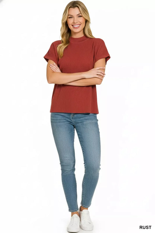 Woman wearing a rust short sleeve ribbed top, skinny blue jeans, and white sneakers, standing against a white background.