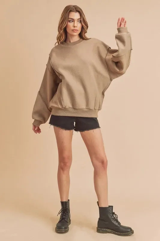 Woman wearing an oversized beige sweatshirt, black cut-off shorts, and black combat boots