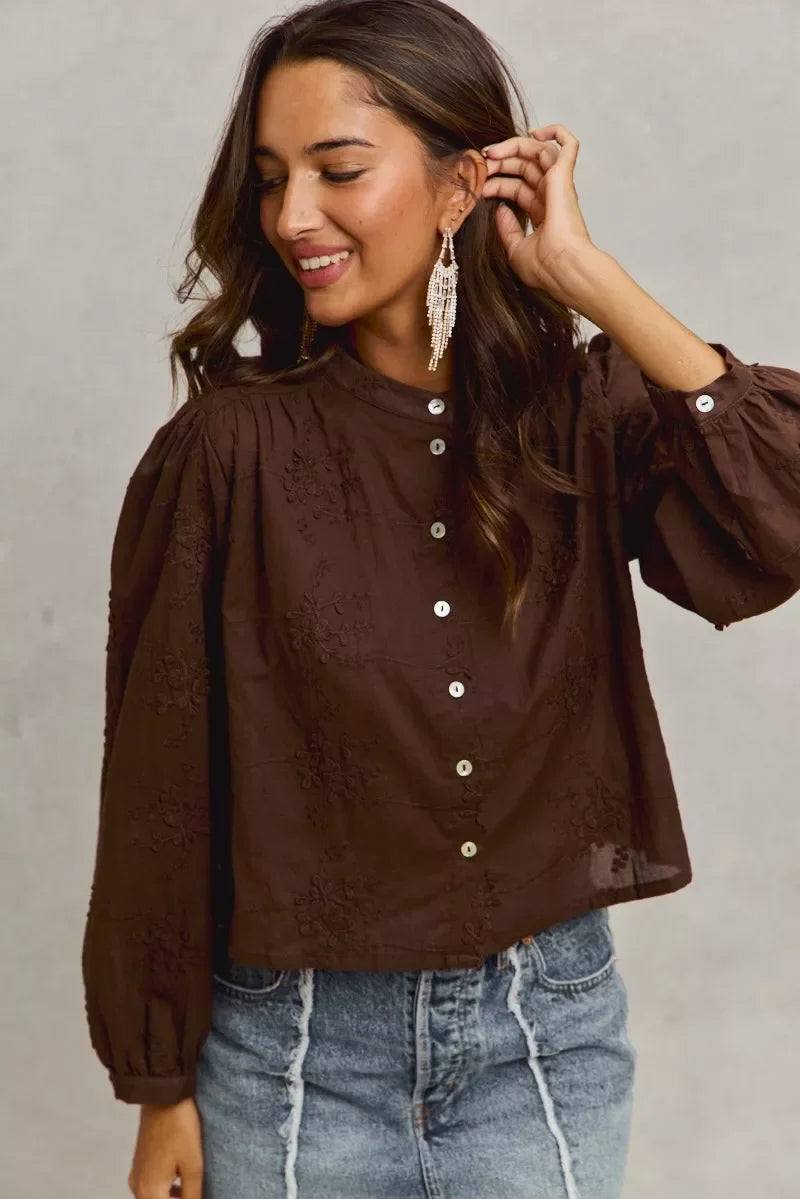 Woman wearing a brown button-up blouse with floral embroidery and puff sleeves, paired with denim skirt