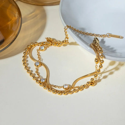 Gold layered bracelet with beads and clear crystals on a neutral background