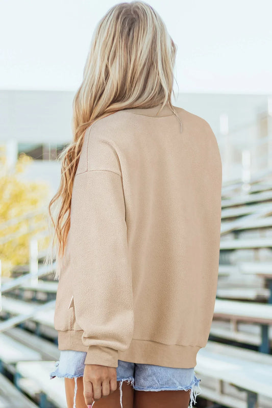 Woman wearing a tan pullover sweatshirt and denim shorts outdoors, shown from the back