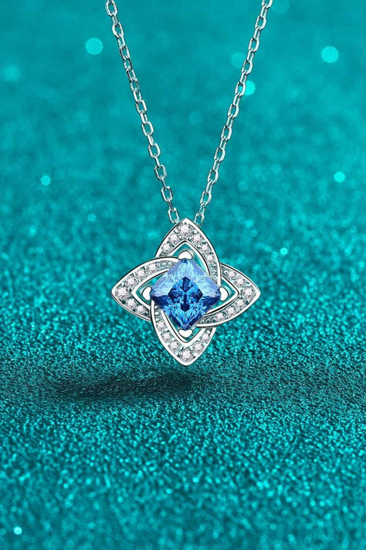 Silver necklace with a blue gemstone pendant and pavé accents on a glittery teal background.