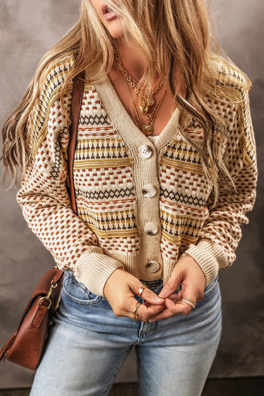 Woman wearing a patterned knit cardigan with large buttons and light-wash jeans.