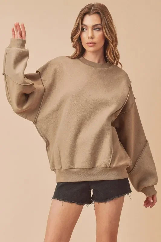 Woman wearing oversized tan sweatshirt with raw edge black shorts, neutral backdrop