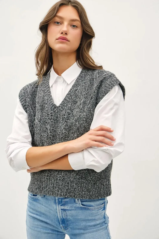 Woman wearing a grey cable knit sweater vest over a white shirt and light blue jeans