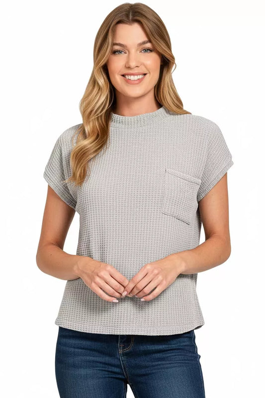 Woman wearing a light grey textured short sleeve top with chest pocket and blue jeans