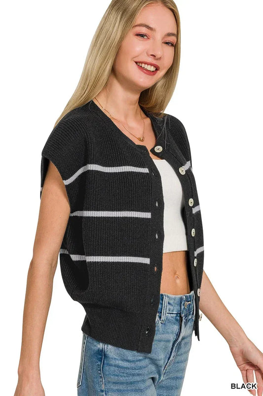 Woman wearing a black knit button-up vest with white stripes, paired with blue jeans.