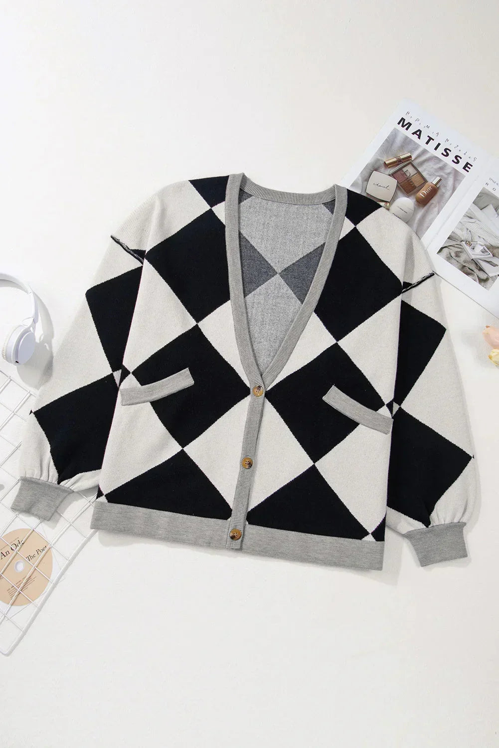Black and white argyle cardigan with grey trim, button front, and pockets, laid flat on white.
