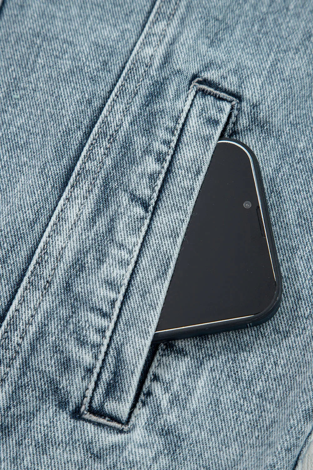 Smartphone in light wash denim pocket, close-up of durable jeans fabric