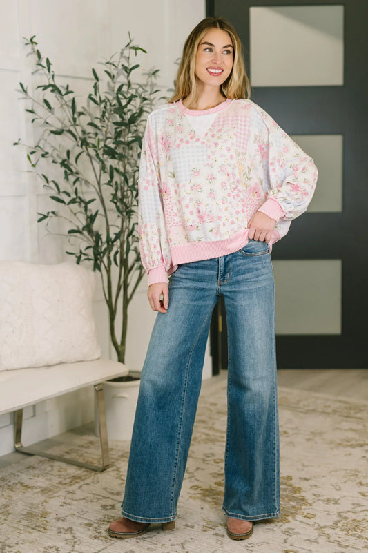 Woman wearing relaxed pink floral patchwork sweater and wide leg jeans indoors