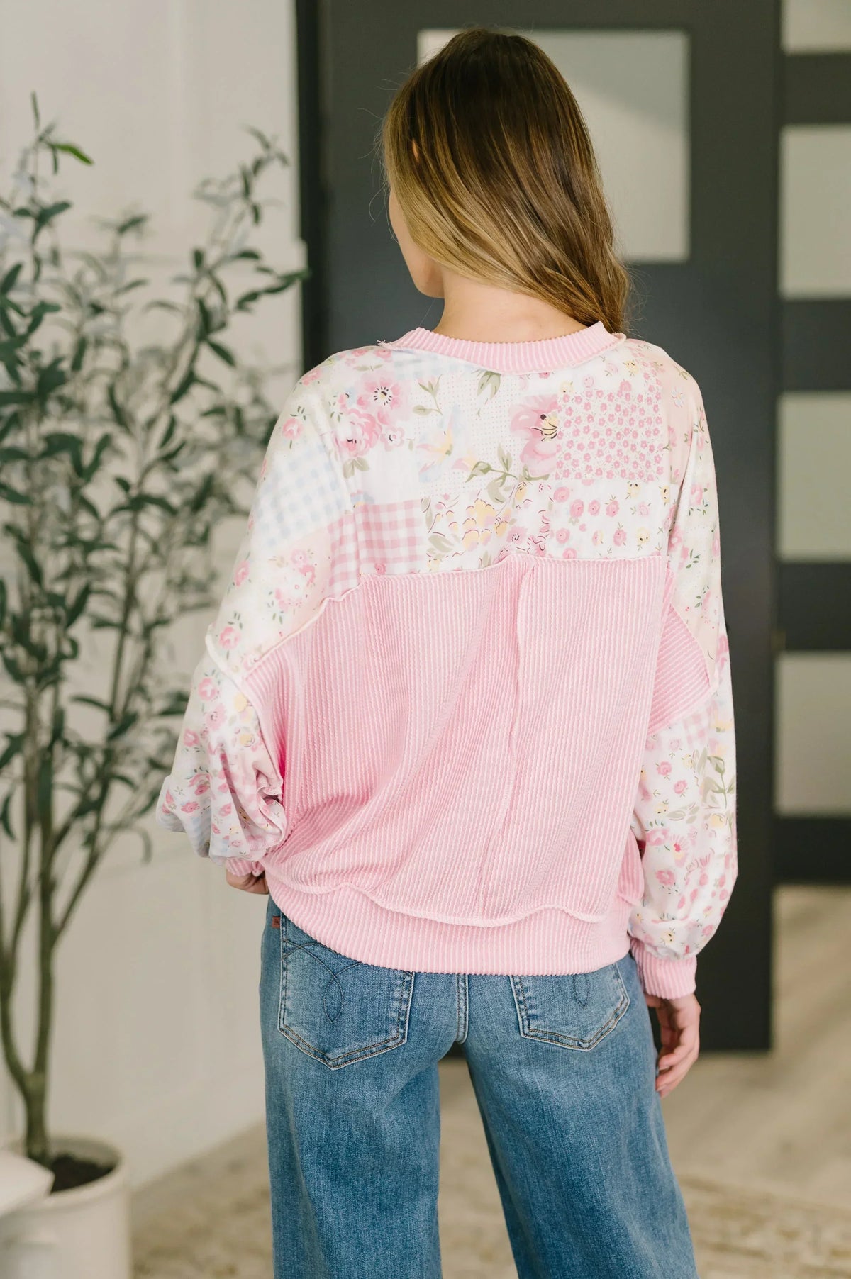Woman wearing a pink patchwork floral top with relaxed fit and blue jeans, back view.