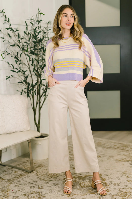 Woman wearing a pastel striped dolman sleeve top and wide-leg cream pants indoors