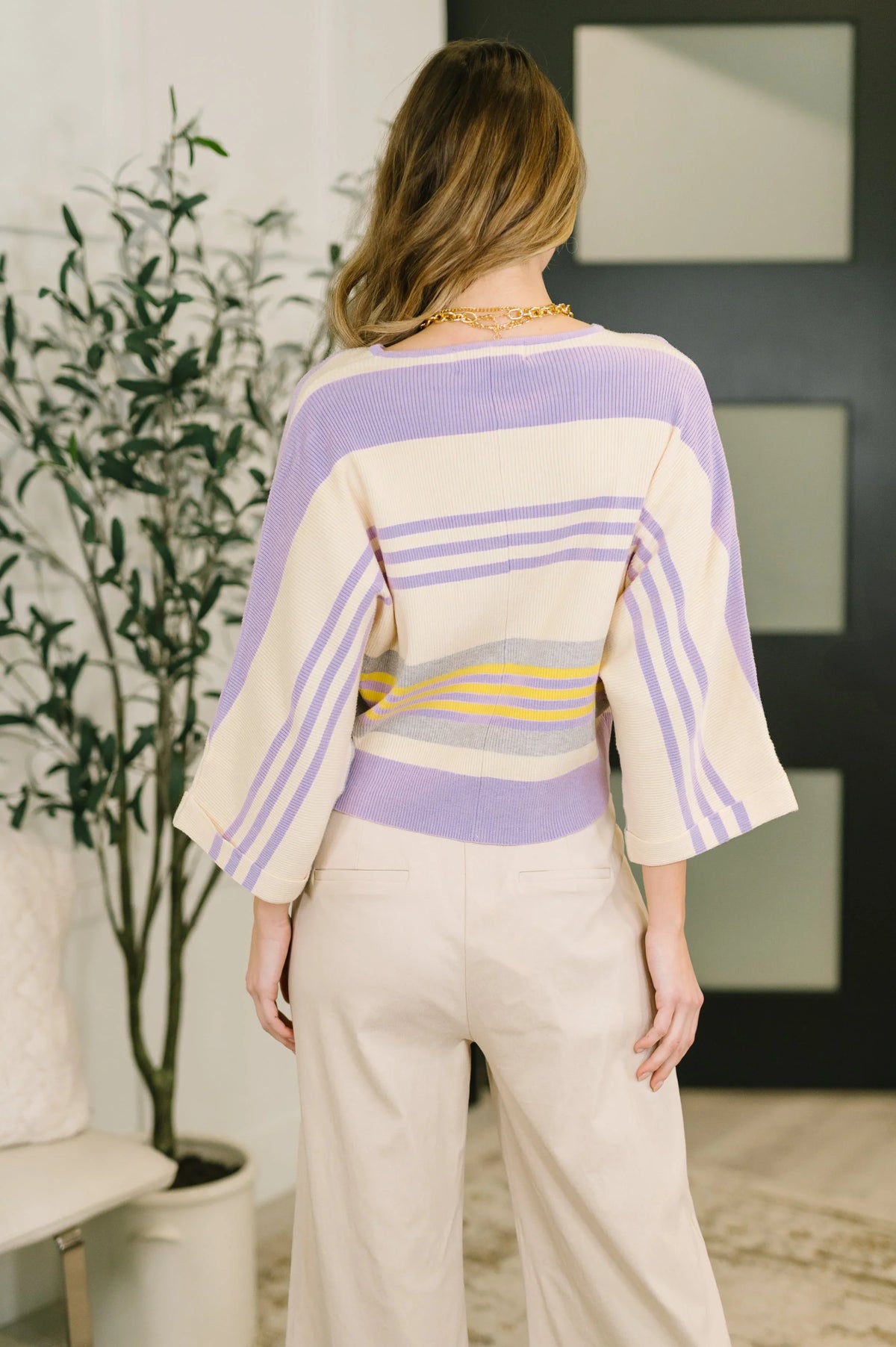 Woman wearing a pastel striped dolman sleeve top and cream wide-leg pants, back view indoors