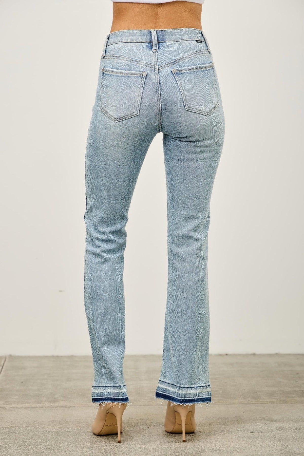 Back view of light wash women's straight leg jeans with raw hem detail, worn with nude heels.