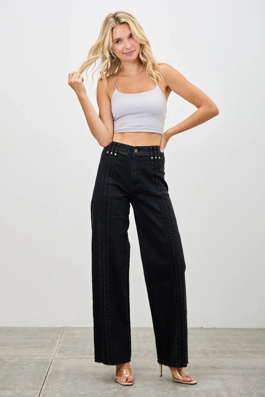 Woman in a white crop top and high-waisted black wide-leg jeans standing on a gray floor