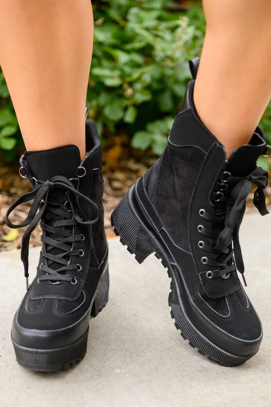 Black lace-up platform combat boots with thick lug soles, worn outdoors on sidewalk.