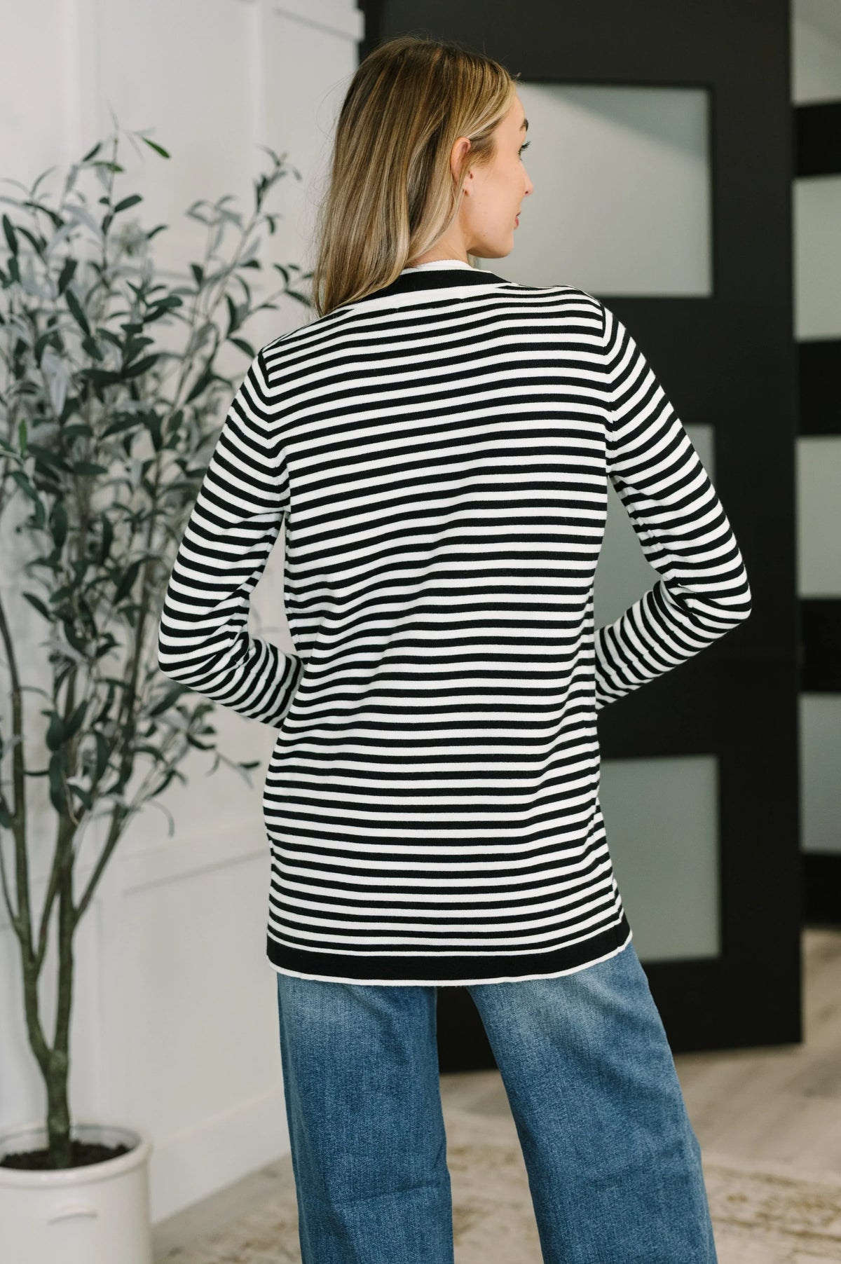 Woman wearing black and white striped cardigan with blue jeans indoors