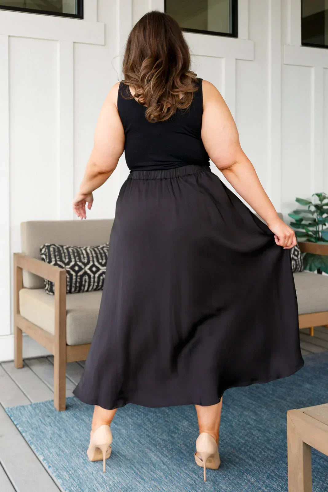 Woman wearing a black sleeveless top and black skirt in an indoor setting.