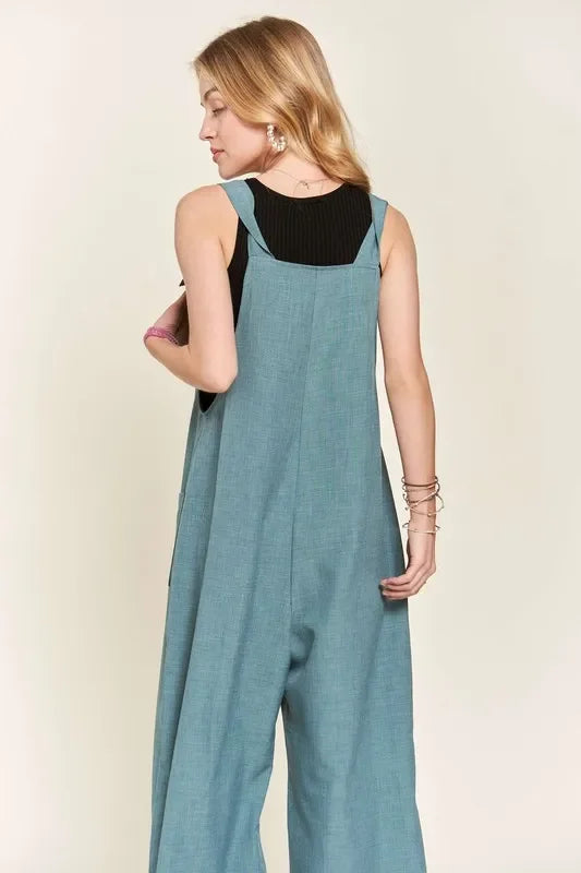 Woman wearing loose blue overall jumpsuit over black sleeveless top, back view