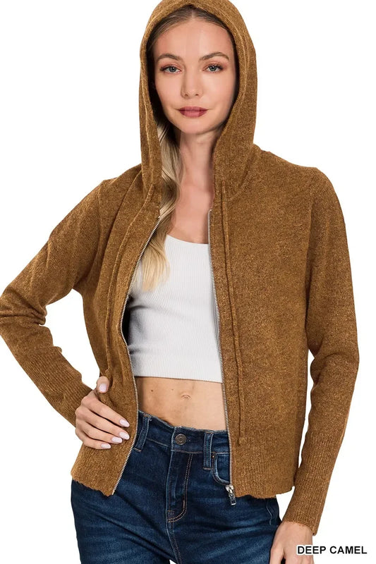Woman wearing a deep camel zip-up hooded sweater with white crop top and blue jeans
