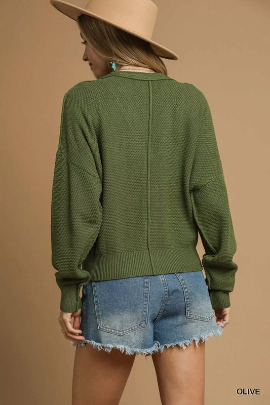 Woman in olive green textured sweater, denim shorts, and tan hat, shown from the back.