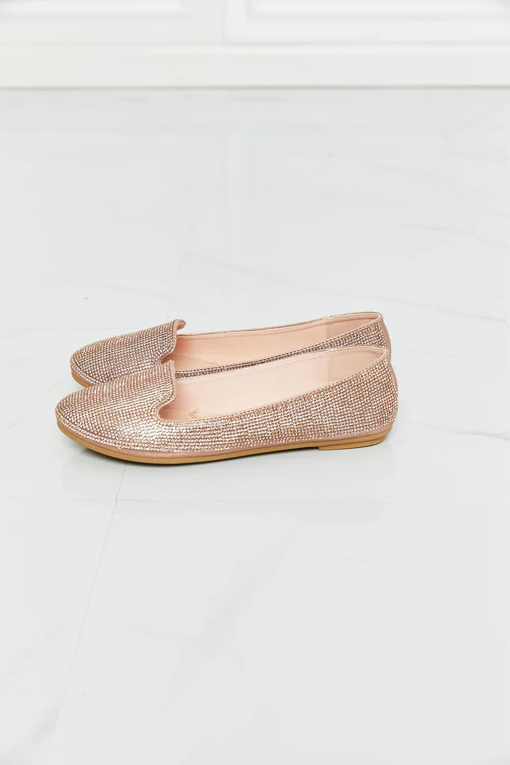 Rose gold rhinestone loafers with flat sole on white marble floor
