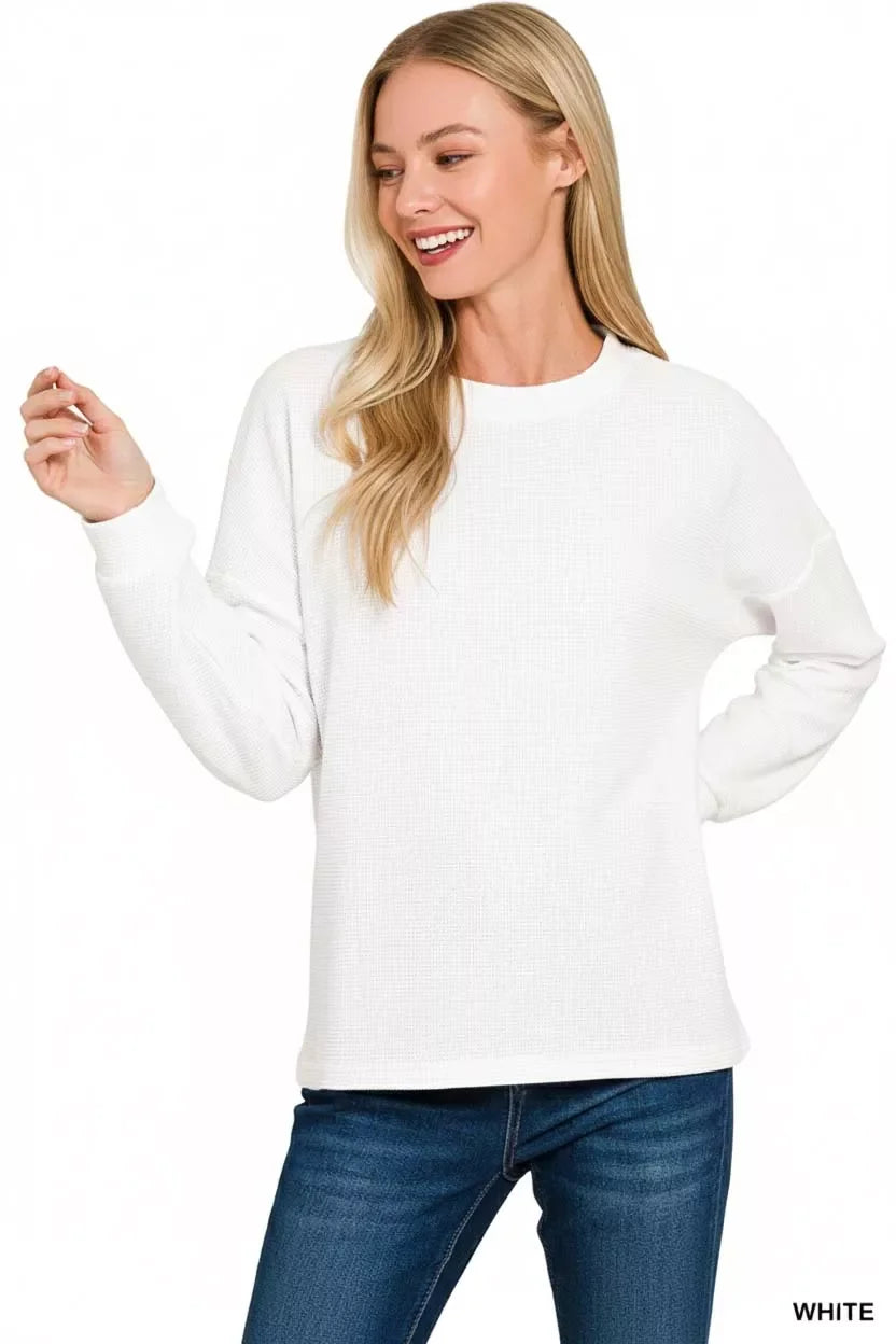 Woman wearing a casual white long sleeve top and blue jeans, relaxed fit, studio background.