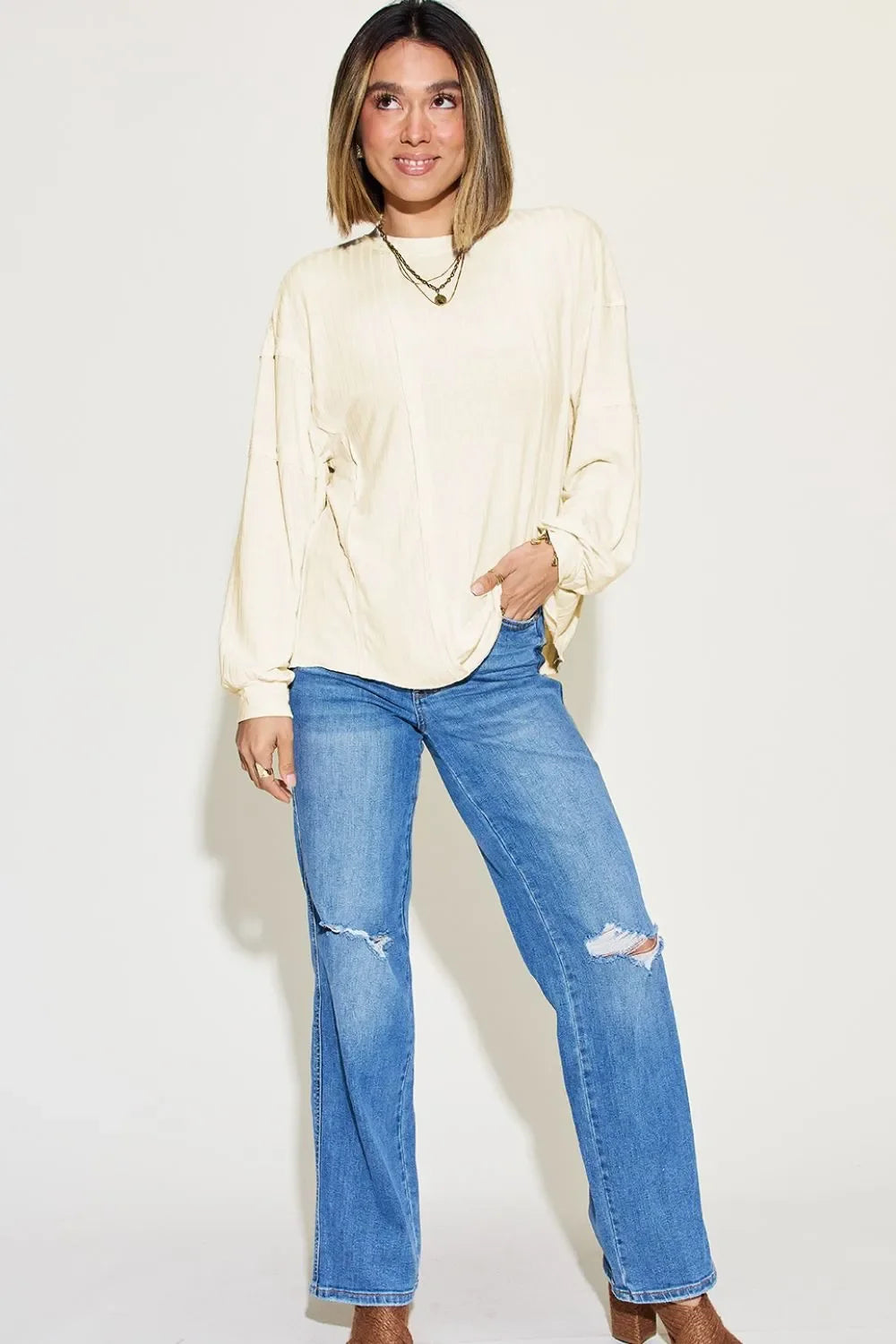 Woman wearing a cream long sleeve blouse and distressed blue jeans, casual minimalist fashion.