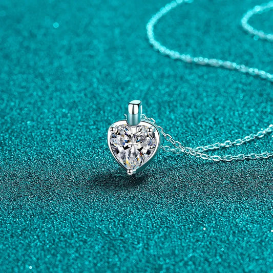 Heart-shaped crystal pendant necklace on a silver chain against teal background