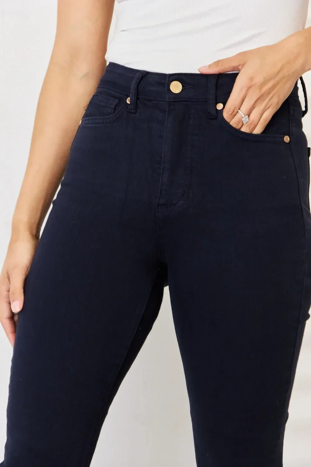 Close-up of woman wearing high-waisted dark denim skinny jeans and white top.