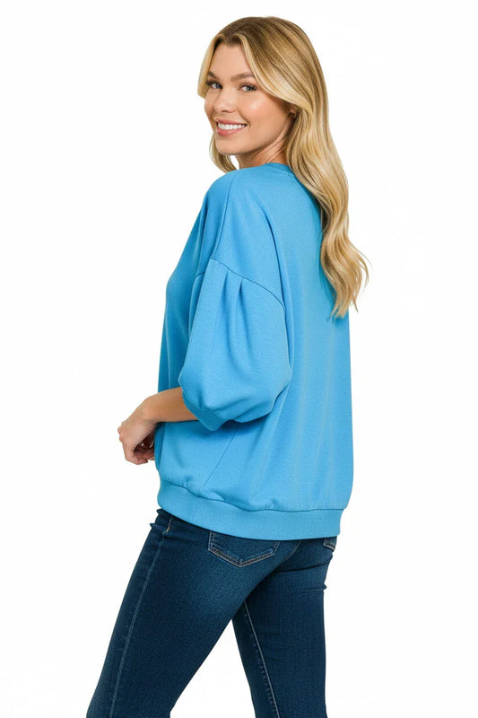 Woman wearing loose blue pullover top with half sleeves and dark denim jeans on white background