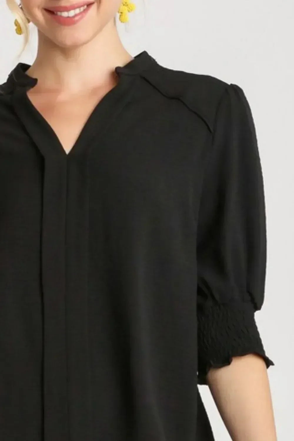 Woman wearing a black V-neck blouse with subtle ruffle collar and smocked half sleeves