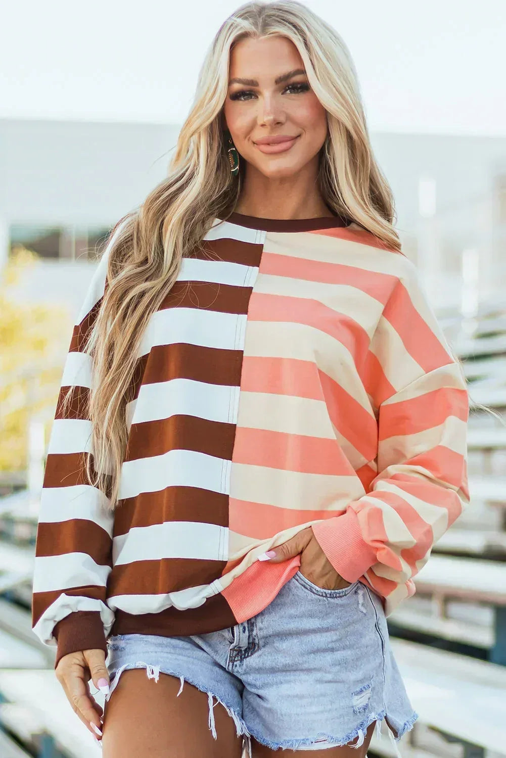 Woman wearing a relaxed striped pullover in brown, white, peach and pink with denim shorts