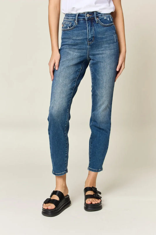 Woman wearing high-waisted blue jeans and black sandals, cropped studio shot.